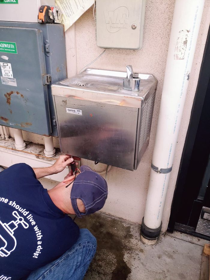 Durbin Plumbing technician in a No One Should Live With a Drip shirt working on a commercial drinking fountain