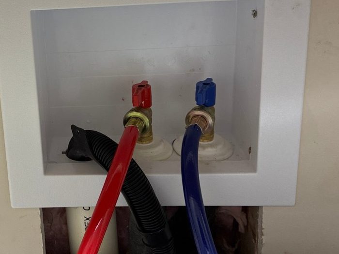 Red and blue supply lines on a washing machine outlet box, from a Durbin Plumbing job